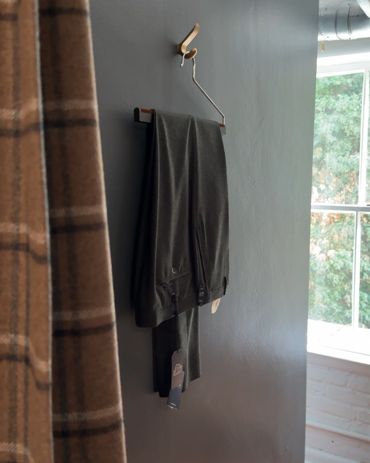 Hanger with trousers on a white wall next to a plaid curtain