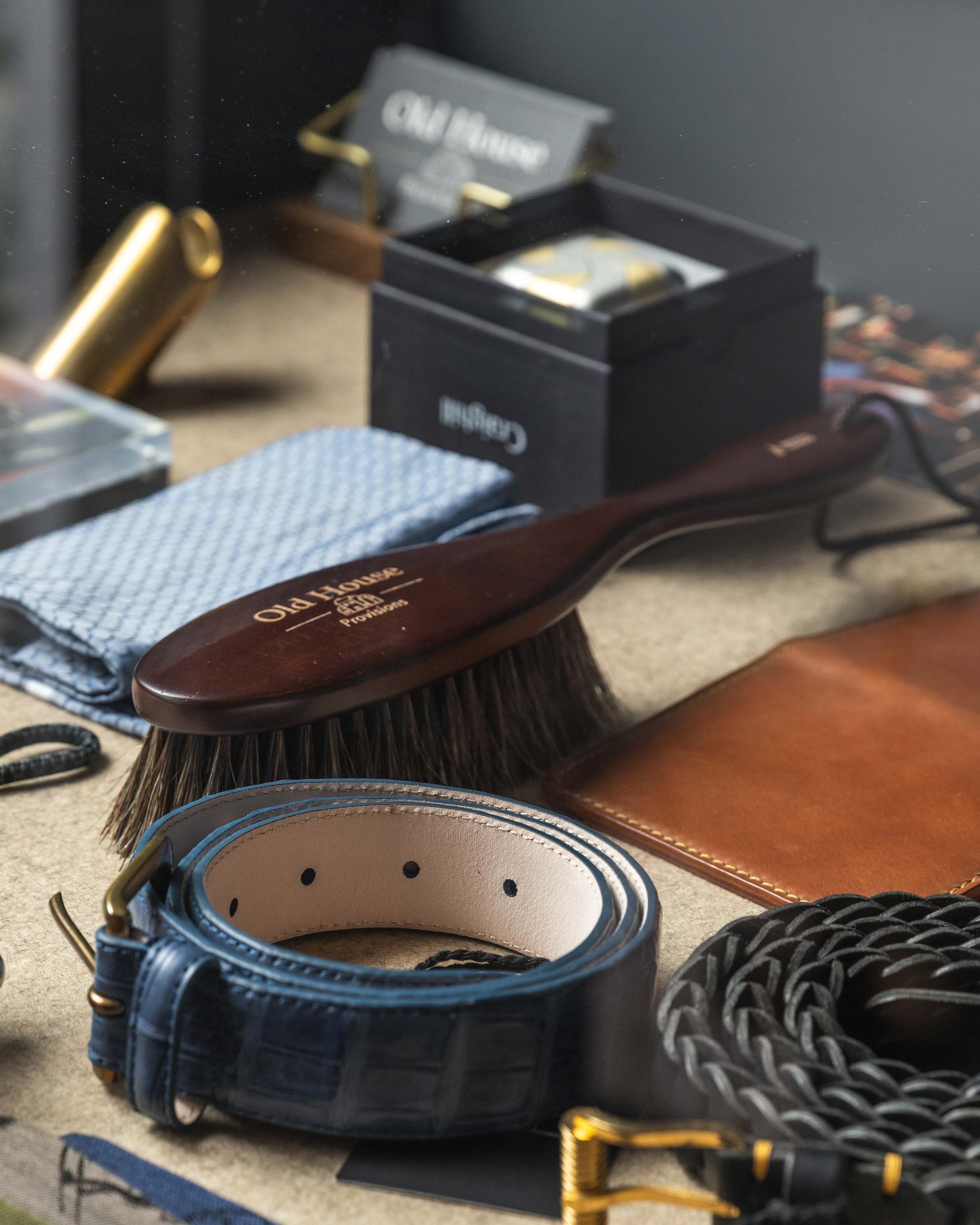 Collection of leather goods including belts, wallets, and a brush on a textured surface.