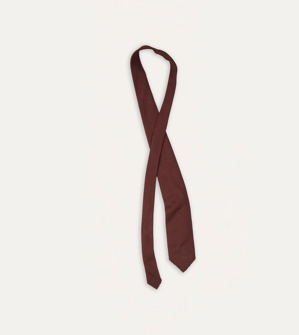 Drake's large knot grenadine handrolled wine tie displayed neatly, showcasing its rich color and classic accessory style.
