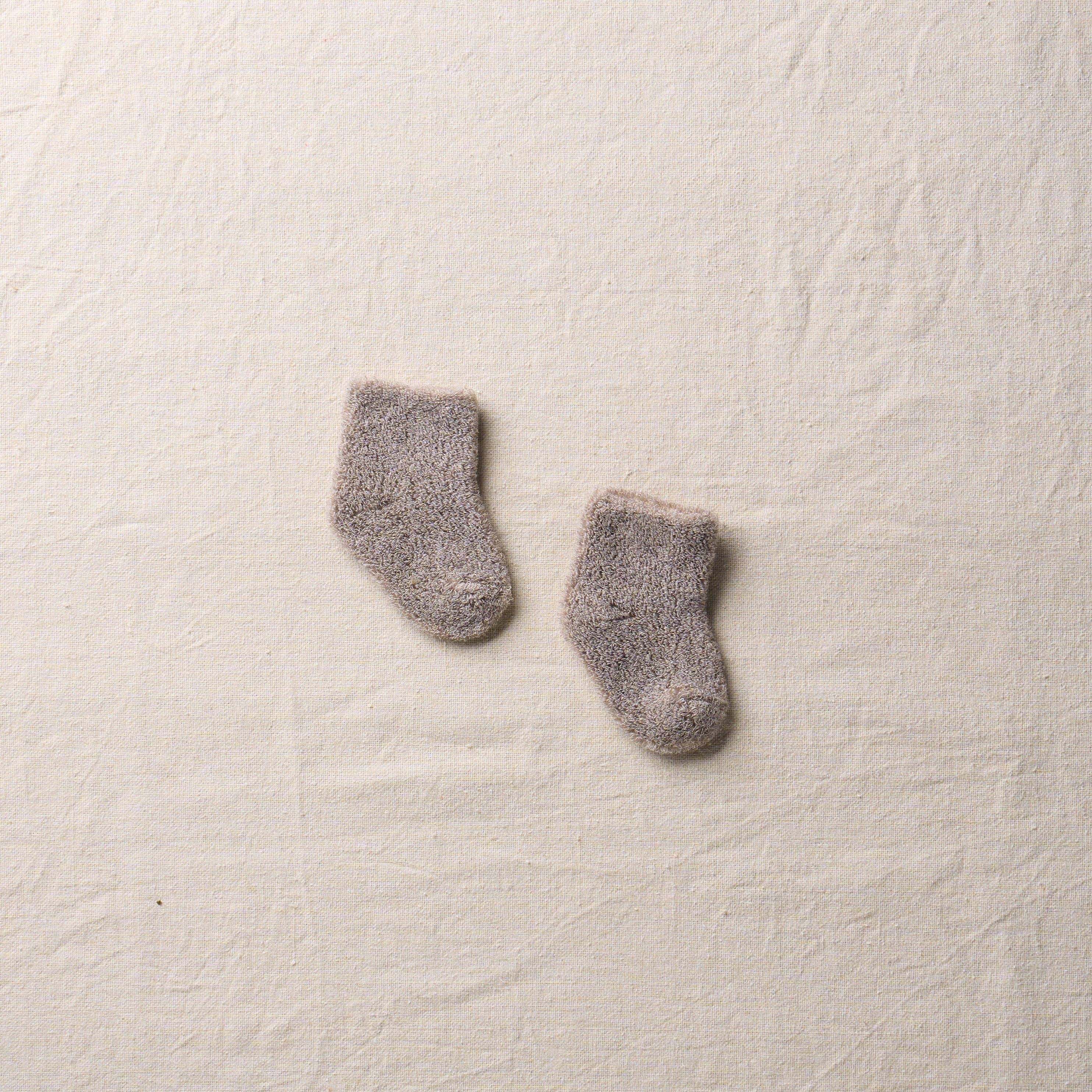 Pair of gray baby socks on a textured beige surface